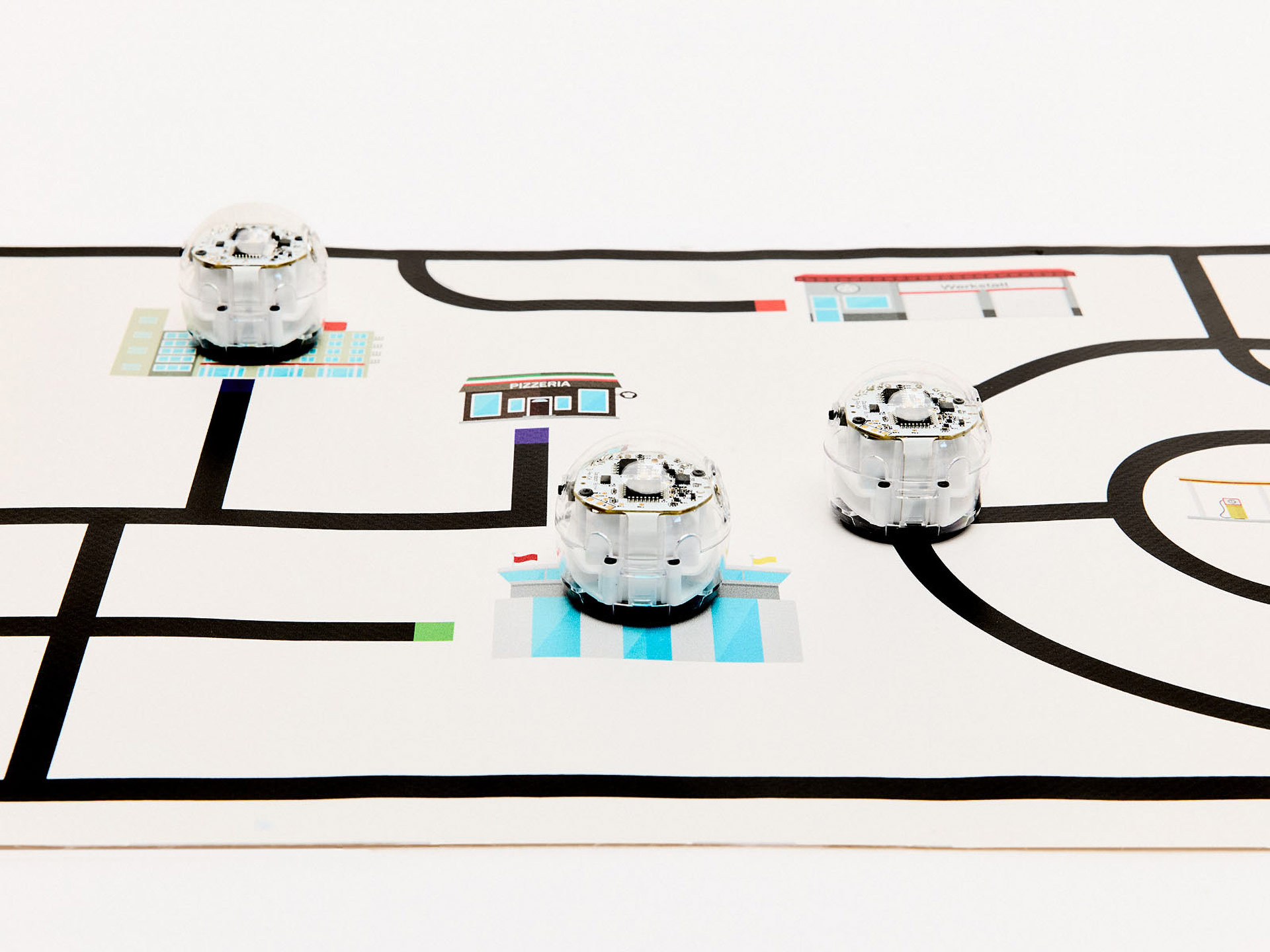 Kleine, runde Roboter mit kleinen Rädern fahren auf Matte, die Informationen in Form von schwarzen Linien und farbigen Codes bereithält.